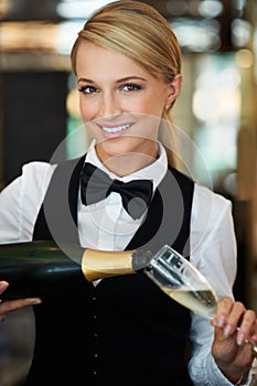 Lets toast to you. Attractive waitress pouring champagne into a champagne glass smiling at the camera.