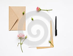 Letter and eco paper envelope on white background. Invitation cards, or love letter with pink roses. Holiday concept, top view, fl