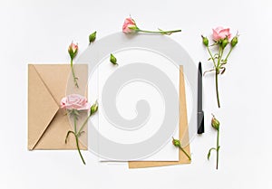 Letter and eco paper envelope on white background. Invitation cards, or love letter with pink roses. Holiday concept, top view, fl