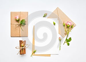 Letter, envelope and gift on white background. Invitation cards, or love letter with pink roses. Holiday concept, top view, flat l