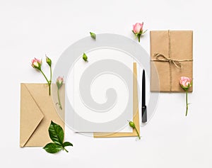 Letter, envelope and gift on white background. Invitation cards, or love letter with pink roses. Holiday concept, top view, flat l