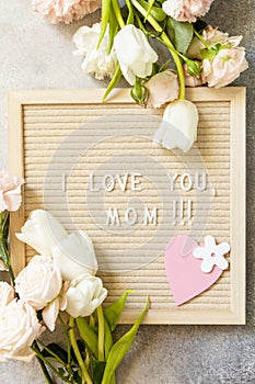 Letter I LOVE MOM with heart on letterboard and beautiful spring flowers.