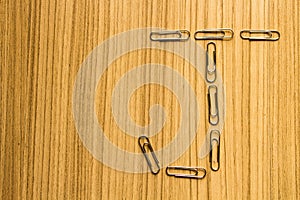 Letter J of paper clip on a wooden brown floor.