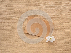 Letter in the sand. Craft paper with a white purple flower on the texture of sea sand. Concept of a beach holiday