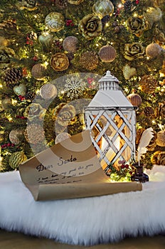 Letter for Santa Claus, ink pen in inkpot and lantern with burning candle against decorated Christmas tree. Child wish list