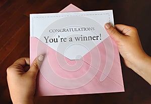 A letter that says Congratulations You`re a winner! with hands holding a pink envelope