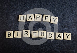 Letter tiles on black slate background spelling happy birthday