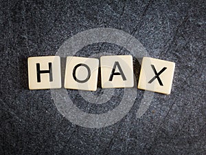 Letter tiles on black slate background spelling Hoax