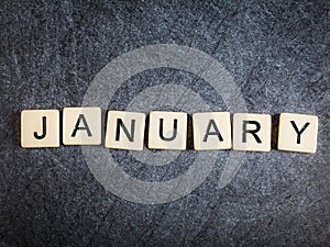 Letter tiles on black slate background spelling January