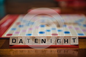Letter tiles spelling out the words date night on stand in the foreground with out of focus game board in the background