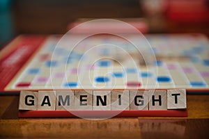 Letter tiles spelling out the words game night on stand in the foreground with out of focus game board in the background