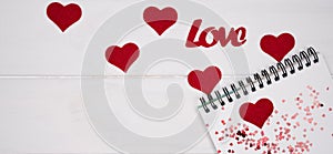 Letter to Valentine`s Day. Blank notepad, red hearts and word Love on white wooden background. Top view. Flatlay. Copy space.