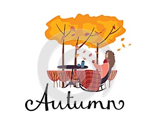Lettering Autumn. A woman sits under a plaid in a cobber chair in the garden and drinks tea