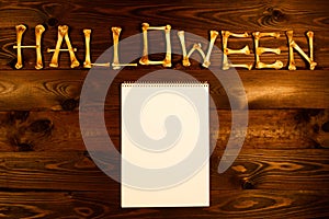 Lettering from the bones of the word Halloween and blank sheet of paper on a dark brown wooden background. Design to celebrate