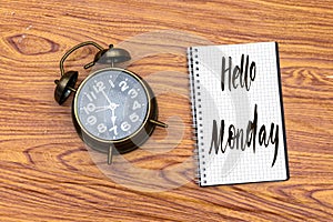 Lettering hello monday on notebook with alarm clock showing 7 o`clock
