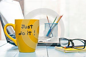 Lettering of inspirational quote JUST DO IT on yellow morning coffee or other hot drink cup at home, business office