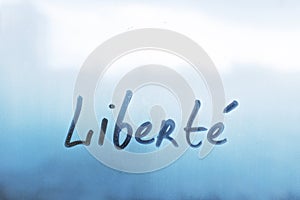lettering Liberte in French is Liberty in english paint with finger with streaks of water on splashed by rain foggy