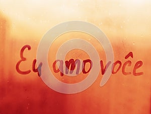 Lettering Portuguese text Eu amo voce I love you in english on sunset wet window