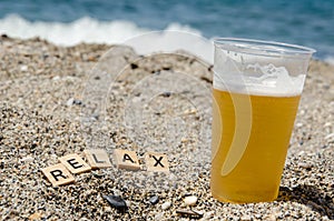 Lettering Relax next to glass of beer on beach against background of blurred turquoise sea. Inscription Relax. Sea vacation