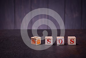 The letters abbreviation sos and fire symbol on wooden cubes, on a dark background, light wooden cubes signs