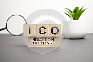 letters of the alphabet of ICO on wooden cubes, green plant on a white background. ICO - short for initial coin offering