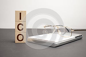 letters of the alphabet of ICO on wooden cubes, green plant on a white background. ICO - short for initial coin offering
