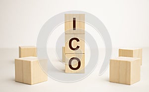 letters of the alphabet of ICO on wooden cubes, green plant on a white background. ICO - short for initial coin offering