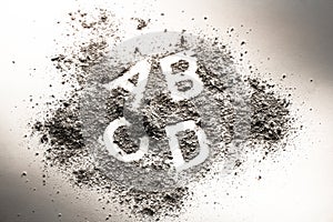 Letters a, b, c, and d written in grey ash, sand, filth or dust