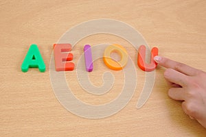 Letters a e i o u and child hand. School concept