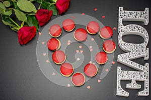 Letters Love on black background with red roses and tasty macaroon