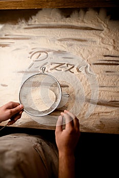 Letters made on flour sifted through a metal sieve on a textured wooden table before making pizza