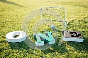 Letters O N E of white, green and black colors lying on a green grass near football goal. Decorations for photos 1 year babies.