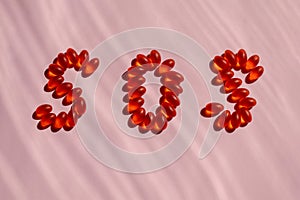 The letters SOS written in orange and red vitamins and pills on a dark pink striped background. Help.