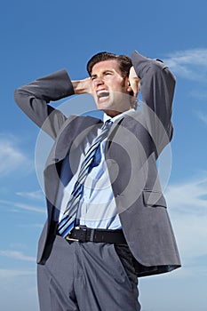 Letting it all out. A frustrated businessman screaming against a blue sky.