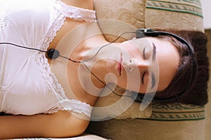 Letting the music wash over her. An attractive young woman listening to music while dozing on the sofa.