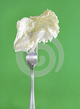 Lettuce leaf on a fork on a green background