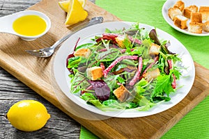 delicious fresh salad of salami and mixed lettuce leaves - baby spinach, arugula, chard in a white dish on the old wooden