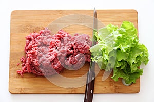 Lettuce salad and ground beef on a cutting board with a knife between them. Plant-based meat concept.