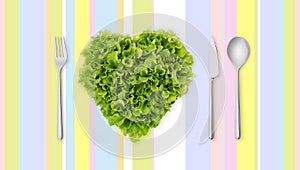 Lettuce in the shape of heart on colored tablecloth with cutlery