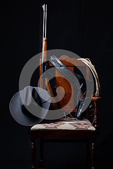 Lever action rifle, revolver, rope, cowboy hat and a chair with a black background