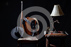 Lever action rifle, revolver, rope, cowboy hat, clock, table, lamp and a chair with a black background