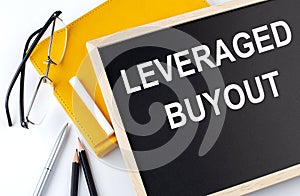 LEVERAGE BUYOUT text on blackboard with notepad , pen, pencil