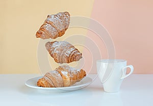 Levitating food, time to wake up call. Flying croissants for breakfast and a cup of coffee, cocao or milk on a beige