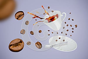 Levitating white porcelain cup with splash of coffee from it, spoon, saucer surrounded by beans on gray-blue background