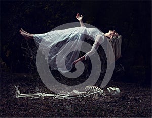 Levitation image of a woman rising from a skeleton on dead leaves photo