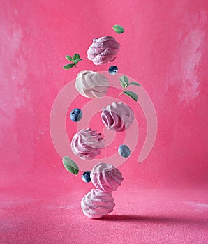 Levitation of marshmallows with blueberries and leaves on a pink background