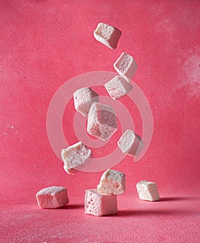 Levitation of white square marshmallows on a pink background