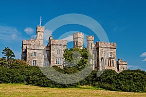 Lews Castle on blue sky in Stornoway, United Kingdom. Castle with green trees on natural landscape. Victorian style photo