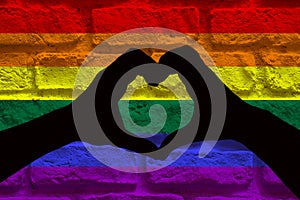 LGBT concept, silhouette of two hands making a heart shape together, on a brick wall with rainbow flag pattern
