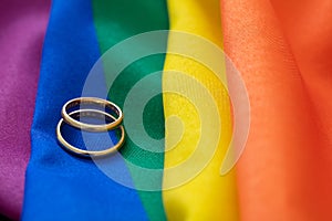 LGBT Gay marriage. Pair of golden rings on rainbow color textile, close up view. Copy space